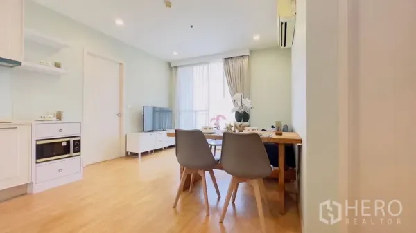 Condominium for rent in Watthana, Bangkok - Bright open-plan living and dining area with light wood floors, white kitchen, TV console and large window.