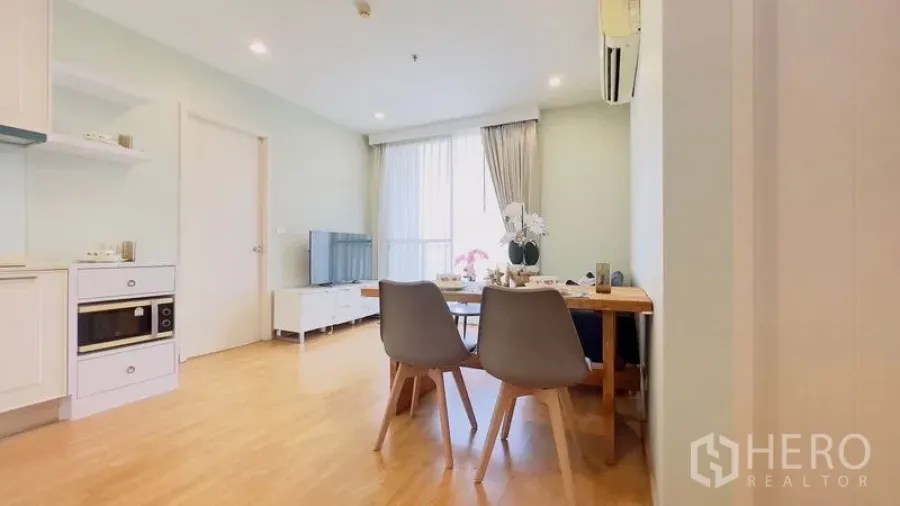 Condominium for rent in Watthana, Bangkok - Bright open-plan living and dining area with light wood floors, white kitchen, TV console and large window.