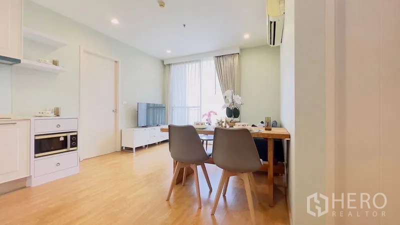 Condominium for rent in Watthana, Bangkok - Bright open-plan living and dining area with light wood floors, white kitchen, TV console and large window.