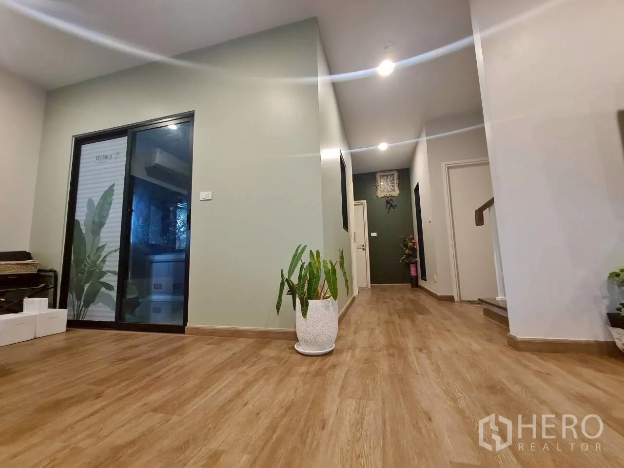 Detached House for rent or sale in Lam Luk Ka, Pathum Thani - Entrance hallway with wood flooring, sliding glass door to the terrace and indoor plants.
