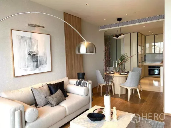 Condominium for rent or sale in Khlong Toei, Bangkok - Open‑plan lounge leading to dining area and kitchen, featuring pendant lights, round table and warm wood floors.