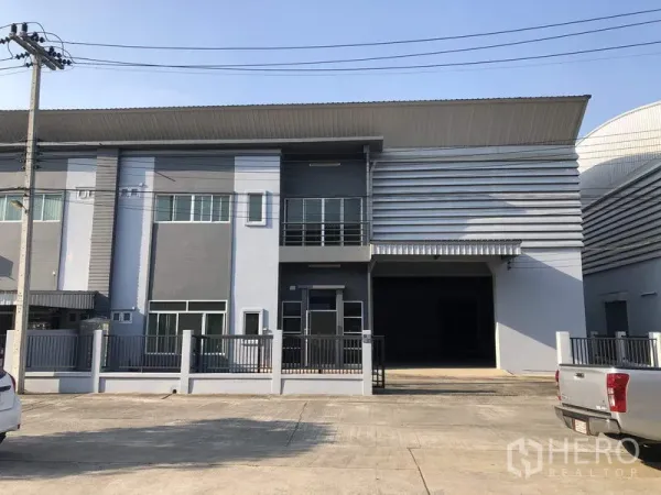 โรงงาน ให้เช่าในLam Luk Ka, Pathum Thani - ด้านหน้าโรงงานสมัยใหม่พร้อมออฟฟิศ 2 ชั้นและประตูม้วนขนาดใหญ่ ภายในโครงการมีรปภ.