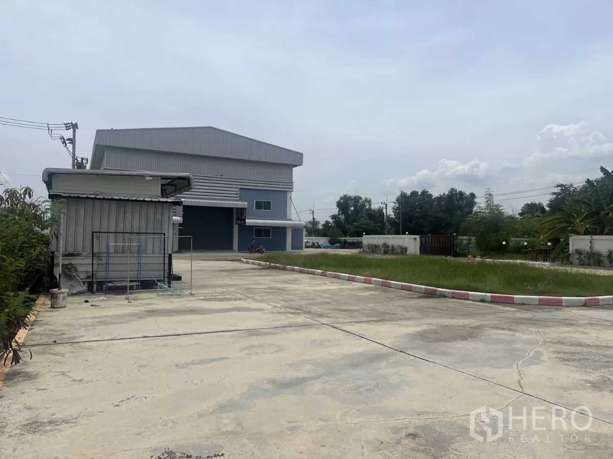 Factory for sale in Lat Lum Kaeo, Pathum Thani - Large paved forecourt and guardhouse in front of the factory with green verge and fencing.
