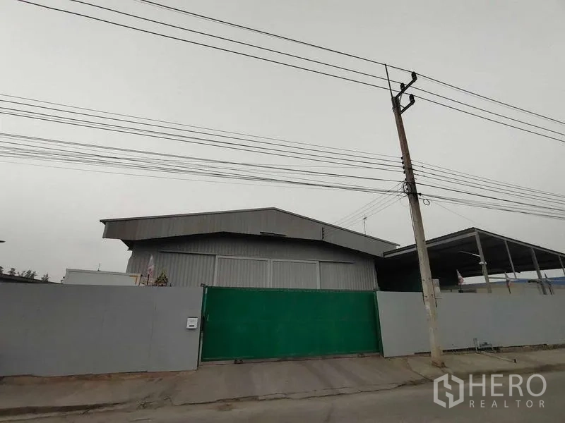 คลังสินค้า ขายในLam Luk Ka, Pathum Thani - ภาพภายนอกโกดังผนังเมทัลชีท ประตูเลื่อนสีเขียว พร้อมสายไฟฟ้าเหนือถนน