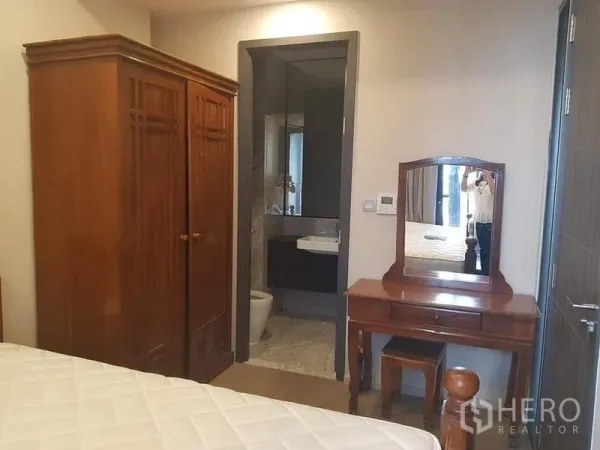 Condominium for rent in Watthana, Bangkok - Bedroom with wooden wardrobe and dressing table leading to a tiled bathroom.