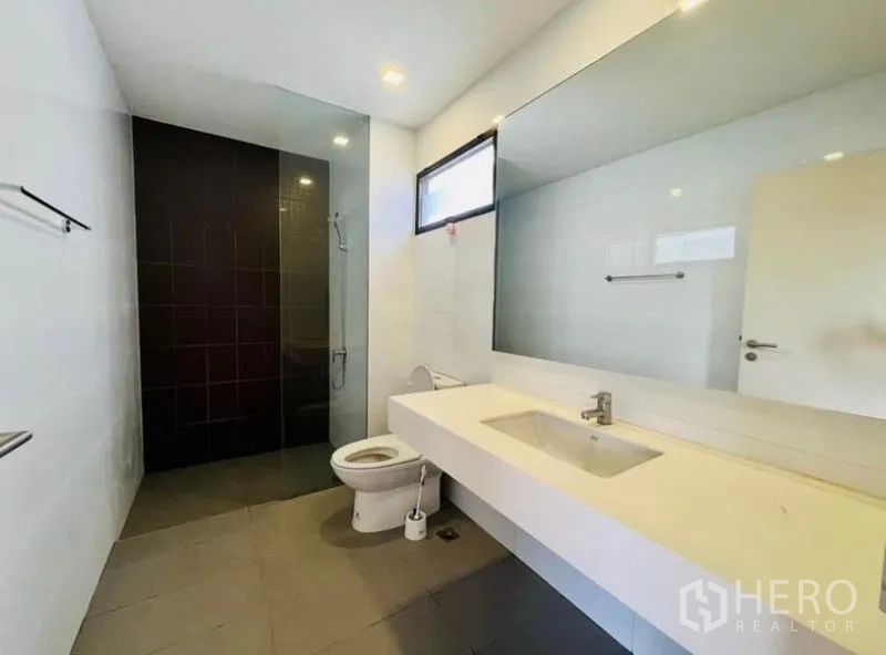 Townhouse for rent in Saphan Sung, Bangkok - Bathroom with long vanity, large mirror, window and glass-enclosed shower area.