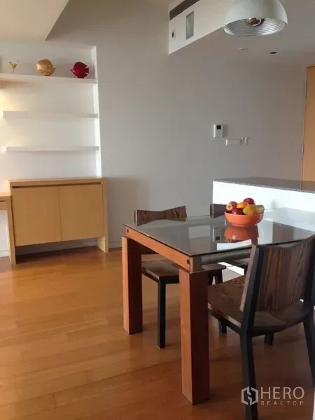 Condominium for rent in Sathon, Bangkok - Bright dining area with a glass-top table, wood floors, and built-in shelves and cabinet in a modern condo.