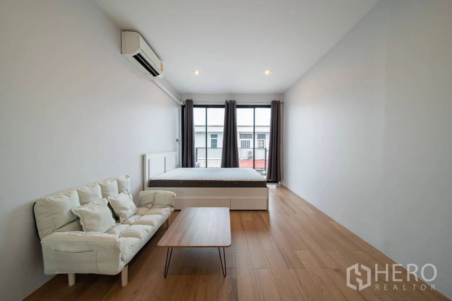 Townhouse for rent in Watthana, Bangkok - Long bedroom with bed, sofa, coffee table and sliding doors to balcony.