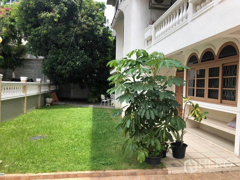 Detached House for rent in Watthana, Bangkok - Green front lawn beside the house with mature tree and arched windows along the facade.