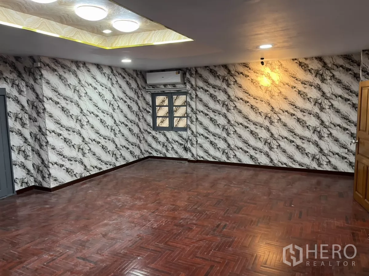 Detached House for rent in Watthana, Bangkok - Expansive living area with parquet floors, marble-effect wallpaper and recessed lighting.