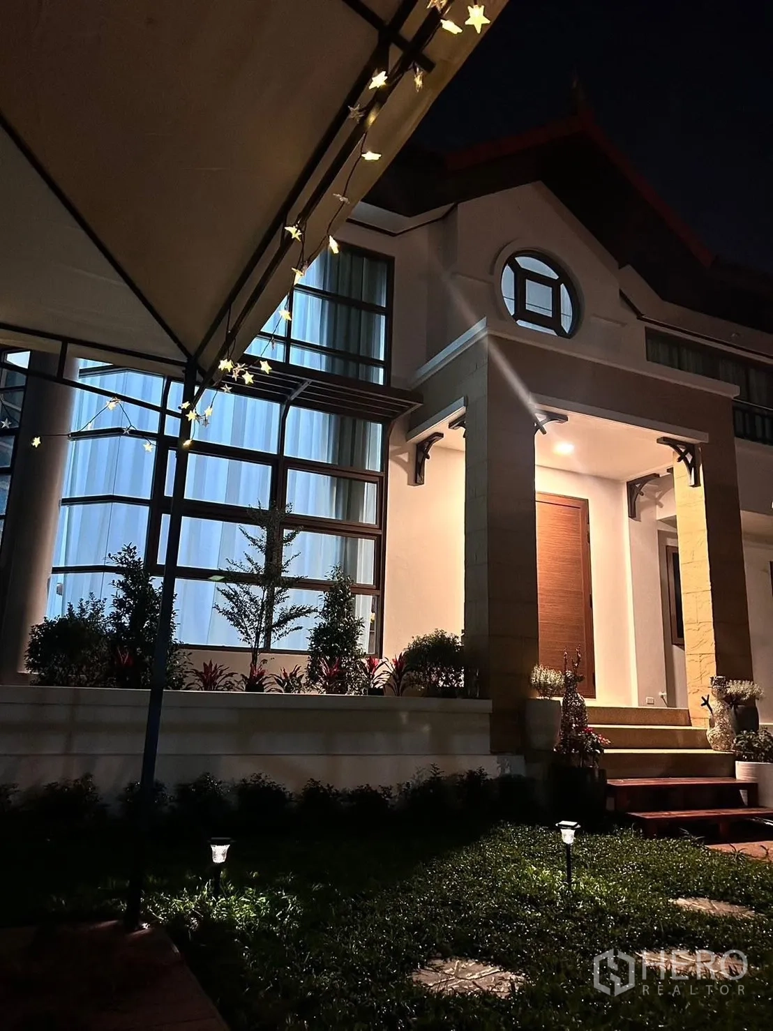Detached House for rent in Lat Krabang, Bangkok - Night view of illuminated house facade with large windows and garden lights.