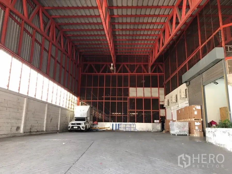 Warehouse for rent in Bang Na, Bangkok - Spacious warehouse loading bay with high red steel trusses, truck access and roller shutter.