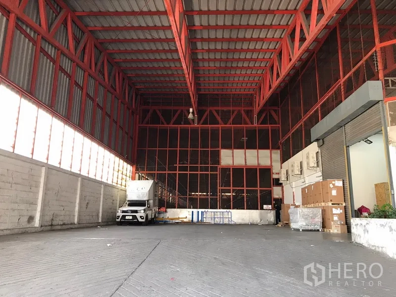 Warehouse for rent in Bang Na, Bangkok - Spacious warehouse loading bay with high red steel trusses, truck access and roller shutter.