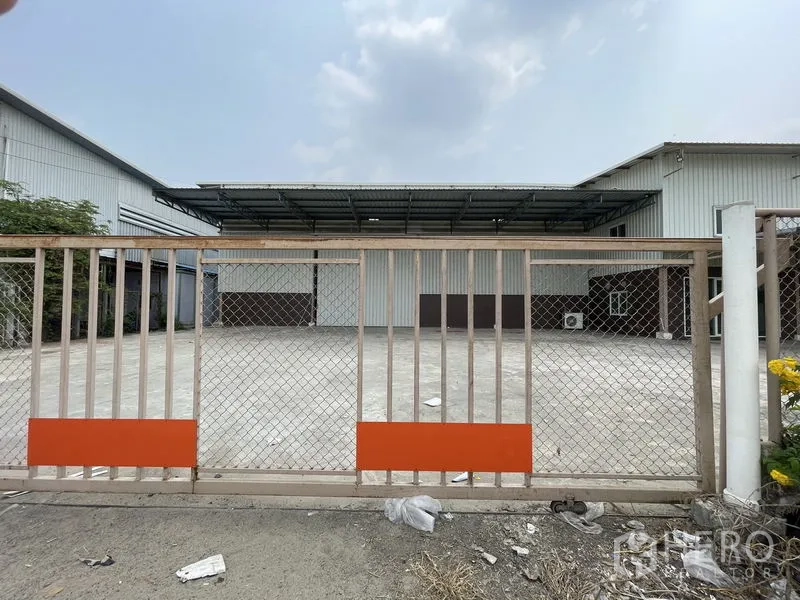货栈 出租在Lat Lum Kaeo, Pathum Thani - 链网推拉大门通向金属外墙仓库前的大型混凝土院场。
