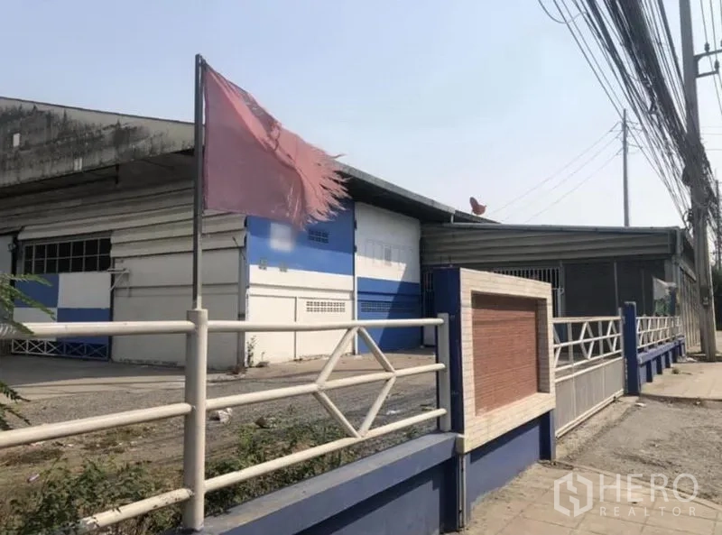 คลังสินค้า ให้เช่าในBang Phli, Samut Prakan - มุมมองริมถนนของโกดังสีฟ้าขาว พร้อมรั้วและสายไฟฟ้าในบางพลี