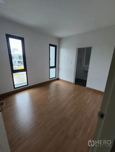 Detached House for rent in Bang Phli, Samut Prakan - Bright bedroom with wood flooring, tall narrow windows and an ensuite door.
