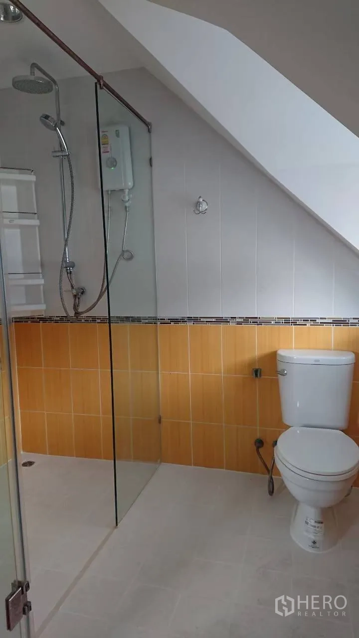 Detached House for rent in Mueang Samut Prakan, Samut Prakan - Bathroom with glass-enclosed shower, water heater and toilet under a sloped ceiling.