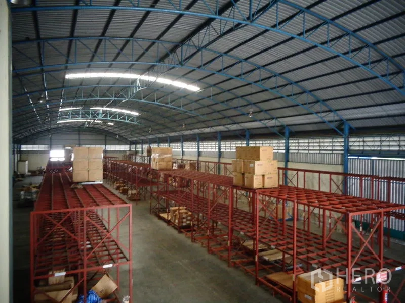 货栈 出租或出售在Lat Lum Kaeo, Pathum Thani - 高挑屋顶仓库，蓝色屋架与装箱的红色货架。