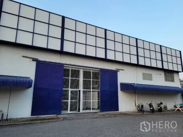 Warehouse for rent in Phra Khanong, Bangkok - Front entrance with blue sliding doors and a secure metal gate