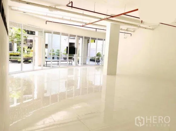 零售空间 出租在Khlong Toei, Bangkok - 明亮的零售室内，抛光瓷砖地面与落地玻璃，可见户外庭院景观。