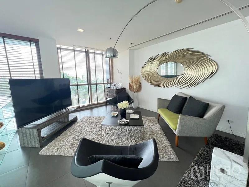 Condominium for sale in Khlong San, Bangkok - Cozy lounge with large TV, shag rug, modern sofa, and sculptural gold mirror.