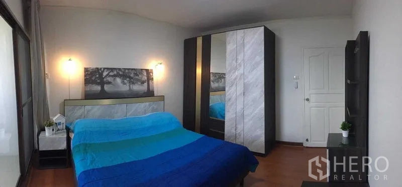 Condominium for rent or sale in Din Daeng, Bangkok - Second bedroom with blue duvet, modern wardrobes, side tables and wall art.