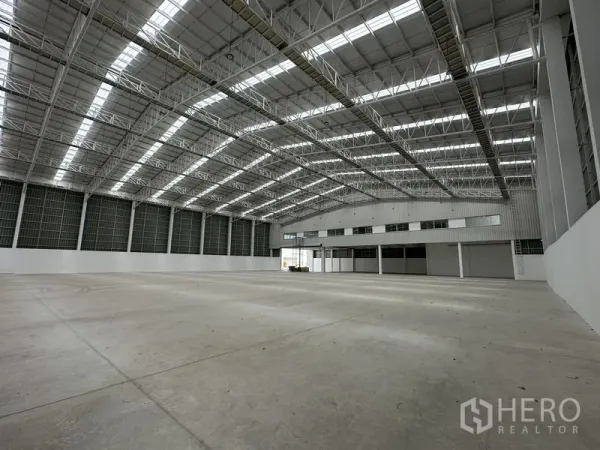 Factory for rent in Pathum Thani - Expansive production hall with high steel truss roof and attached office block.