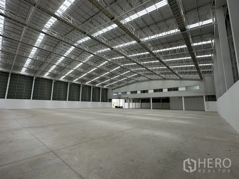 Factory for rent in Pathum Thani - Expansive production hall with high steel truss roof and attached office block.