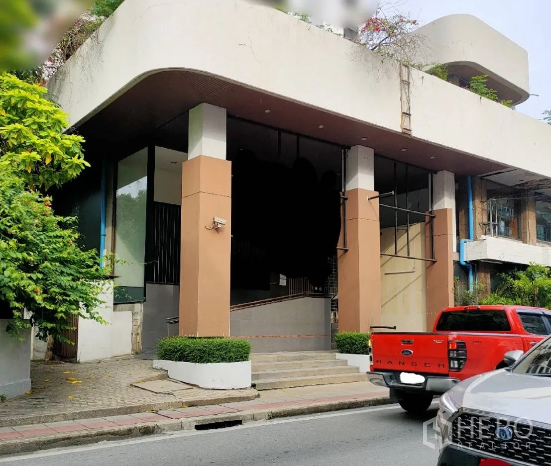 零售空间 出租在Watthana, Bangkok - 现代商用建筑外观，挑高玻璃立面、雨棚、台阶与坡道，绿化及街景，位于曼谷瓦他那区。