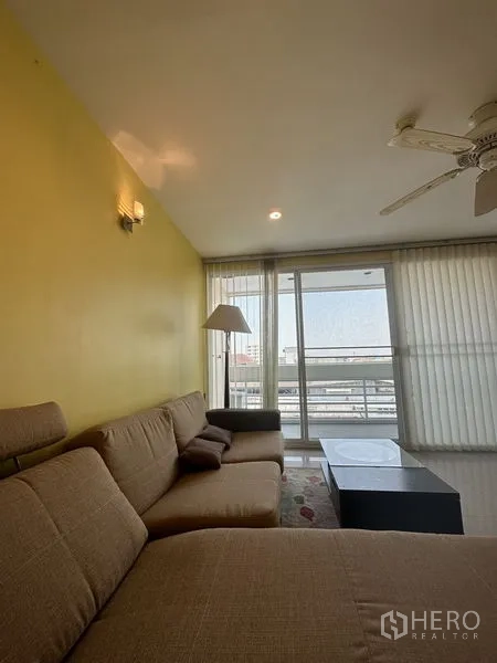 公寓 出售在Watthana, Bangkok - 客厅配L型沙发与落地灯，落地推拉门通往观景阳台。