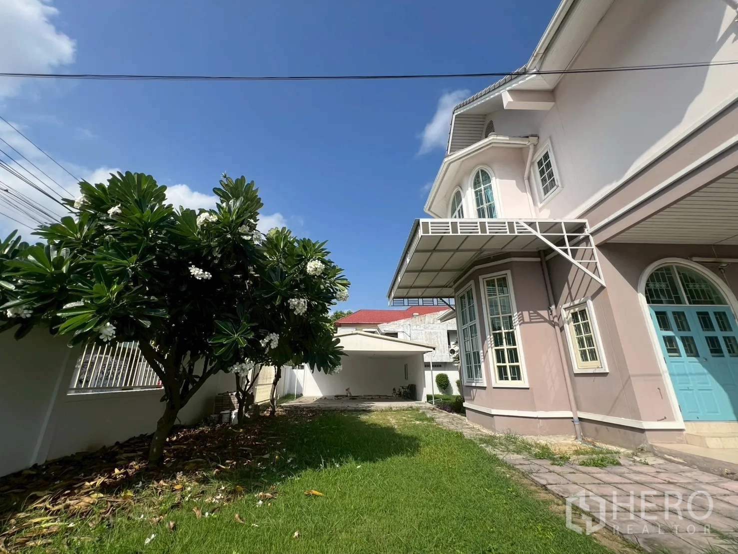 独立式住宅 出售在Phra Khanong, Bangkok - 侧院草地与小径，通向蓝色入户门和飘窗。