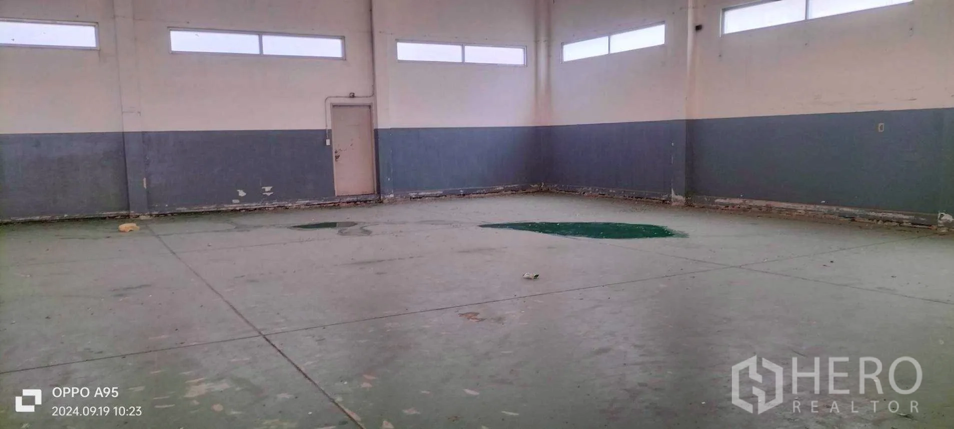 Factory for rent in Khlong Luang, Pathum Thani - Open floor area with patches on green epoxy surface near a side service door.