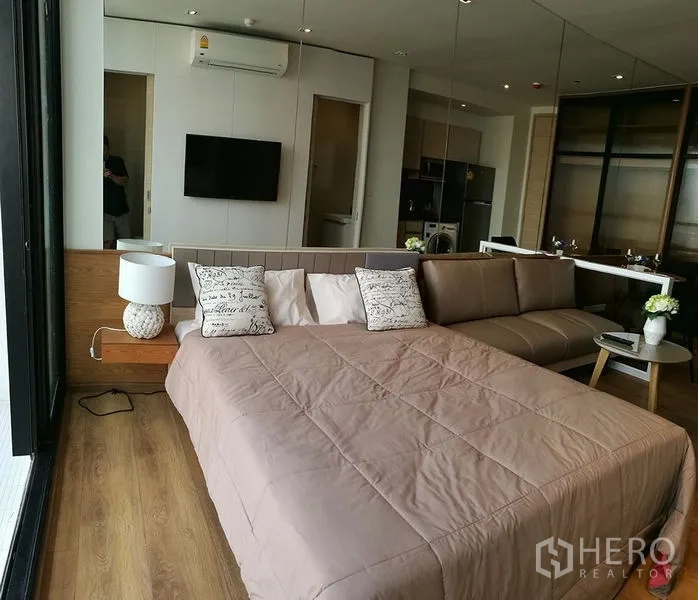 Condominium for sale in Khlong Toei, Bangkok - Bright 1-bedroom condo with bed, sofa, wall-mounted TV, wood floors and large windows.