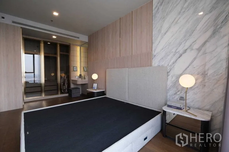Condominium for rent in Khlong Toei, Bangkok - Spacious master suite with marble accent wall and mirrored wardrobes.