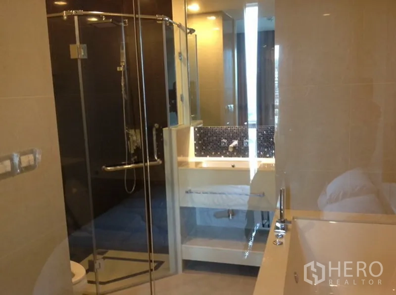 Condominium for rent in Ratchathewi, Bangkok - Bathroom with glass-enclosed shower, bathtub and mirrored vanity.