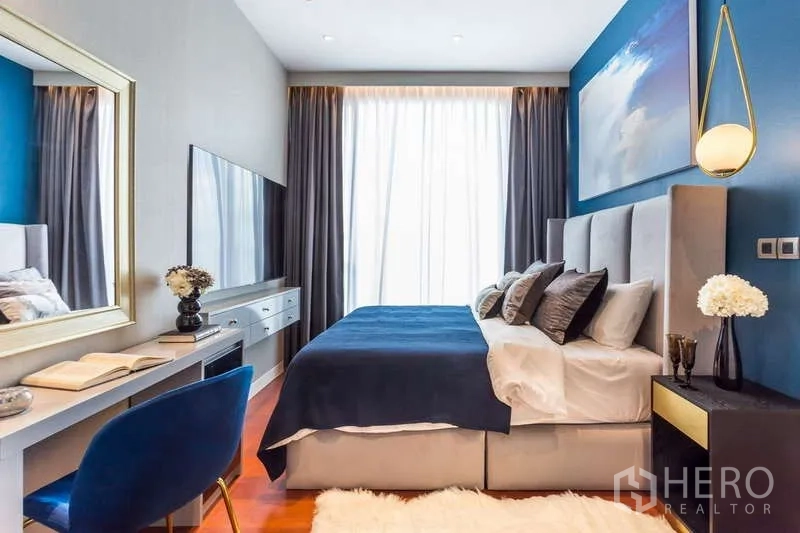 คอนโด ให้เช่าในWatthana, Bangkok - ห้องนอนผนังสีน้ำเงิน เตียงบุผ้า โต๊ะทำงาน ทีวีติดผนัง และหน้าต่างสูง