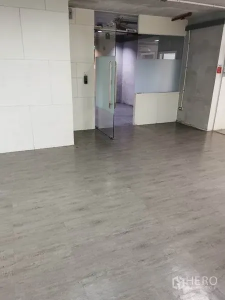 办公空间 出租在Khlong Toei, Bangkok - 开放式办公室内景，灰色乙烯基地板、白色墙面、玻璃入户门与磨砂隔断，顶部为外露管线。