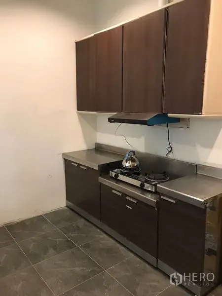 Townhouse for rent or sale in Phra Khanong, Bangkok - Compact kitchen with dark wood cabinets, stainless counters, gas hob and hood.
