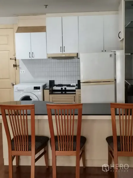 公寓 出租在Pathum Wan, Bangkok - 吧台配三把木椅，对面是带炉灶、烟机、冰箱与洗衣机的整体厨房。