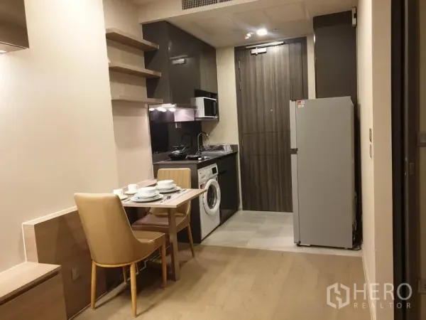 Condominium for rent in Watthana, Bangkok - Compact kitchenette with built-in cabinets, microwave, washer, fridge and two-seat dining table.