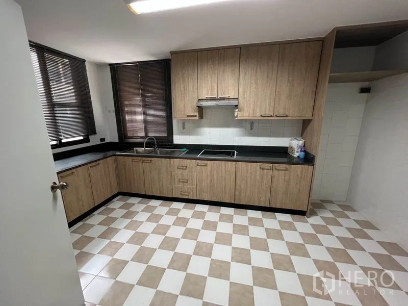 Condominium for rent or sale in Watthana, Bangkok - Closed kitchen with L-shaped wood cabinets, black countertops, sink, cooktop and range hood.