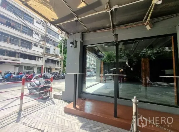 零售空间 出租在Bang Rak, Bangkok - 临街玻璃店面，木质小平台与遮棚，巷道边停着摩托车。
