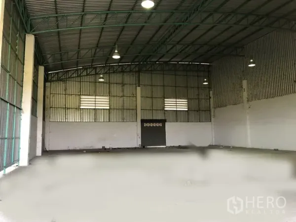 工厂 出租在Pathum Thani - 仓库内部空间宽敞，钢结构高屋顶，吊灯照明，混凝土地面与通风窗。