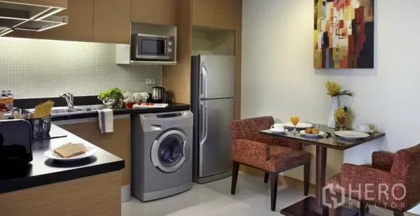 Condominium for rent in Khlong Toei, Bangkok - Compact fitted kitchen with fridge, microwave, sink, washing machine and a two-seat dining nook.