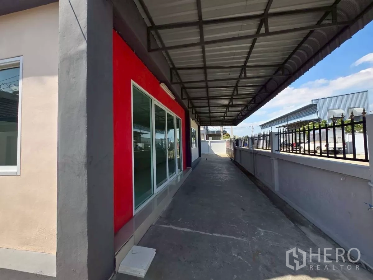 Factory for rent or sale in Mueang Samut Sakhon, Samut Sakhon - Covered side walkway with metal roof along the glass-fronted office and perimeter fence of the factory.