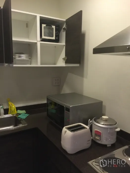 Condominium for rent in Bang Kho Laem, Bangkok - Kitchen countertop with microwave, toaster, rice cooker and open wall cabinets.