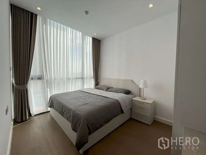 Condominium for rent or sale in Sathon, Bangkok - Bright bedroom with floor-to-ceiling windows, sheer curtains and a queen bed.