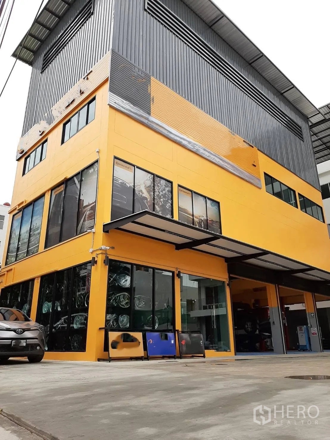 Home Office for rent in Phra Khanong, Bangkok - Corner view of the yellow building with large glass windows and a covered entrance.