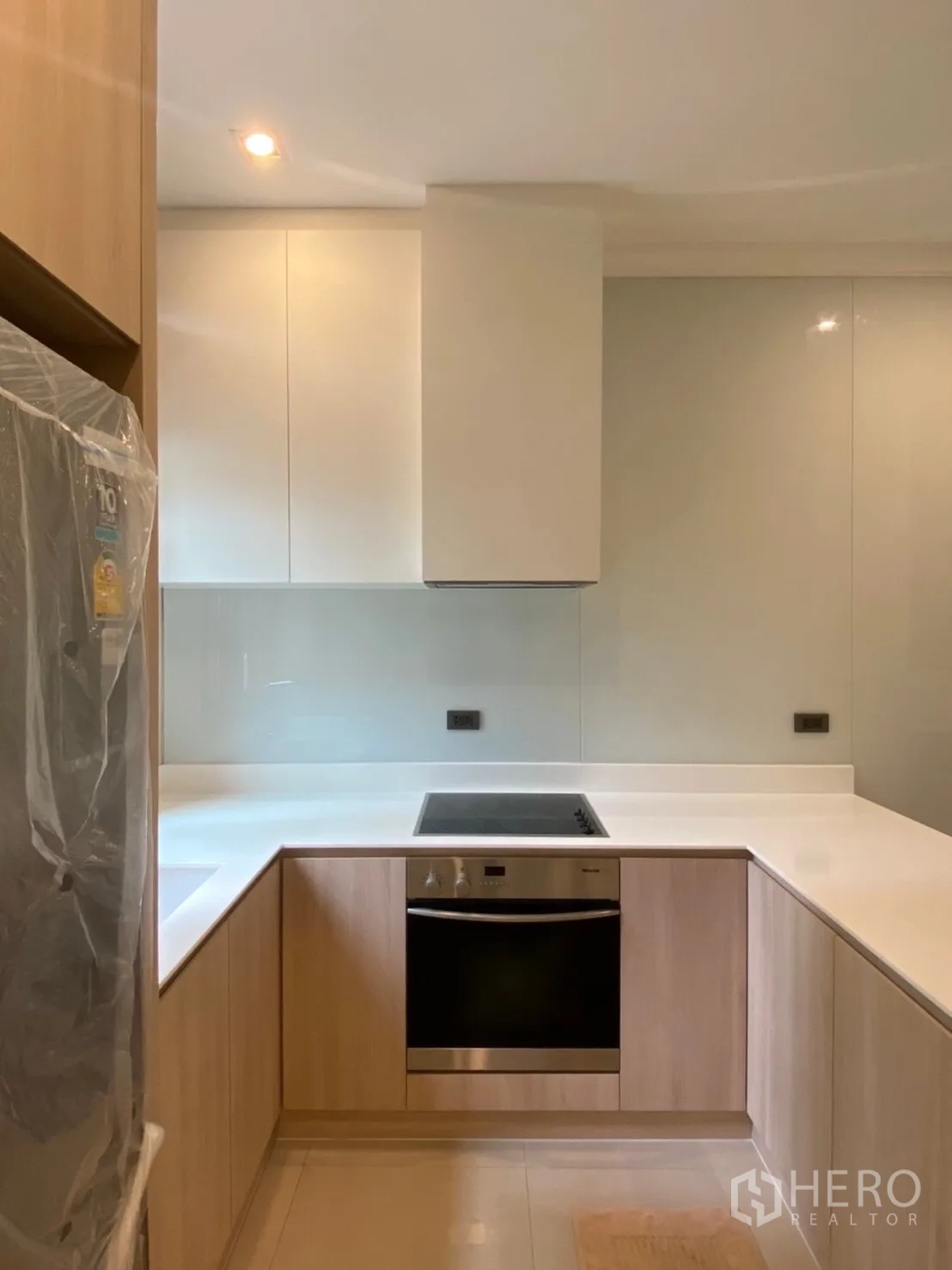Detached House for rent in Bang Phli, Samut Prakan - U-shaped modern kitchen with light wood cabinets, white countertop, built-in oven and induction hob.