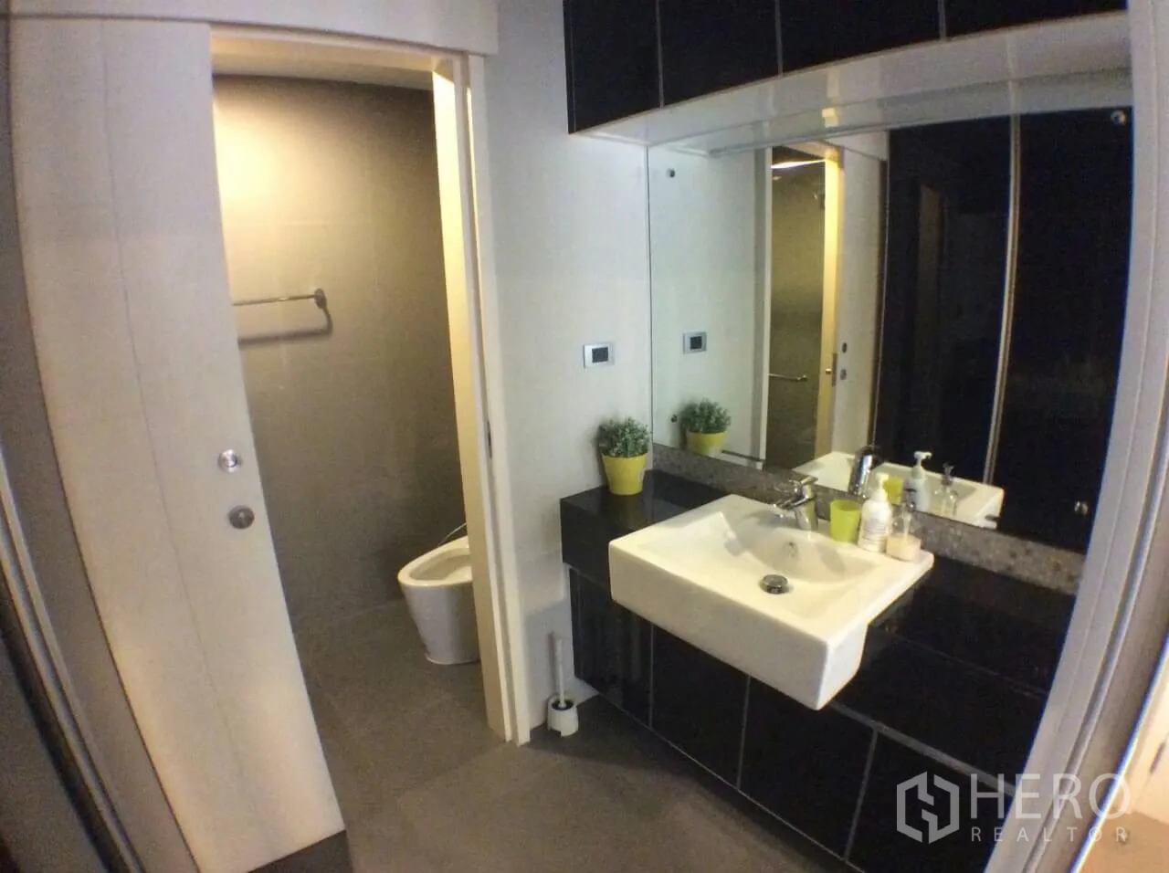 Condominium for rent in Khlong Toei, Bangkok - Modern bathroom with large mirror, square basin, and separate toilet area with gray tiles.